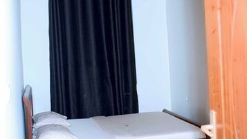 A small, single-bed room with a wooden headboard, a black curtain, and a wooden door.