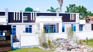 A modern two-story building with a white facade, large windows, and a landscaped front yard with a rock garden. - The Moon Crib (Gisenyi)