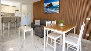 A modern living room with a dining area, a kitchen in the background, and a wooden wall with a picture. - Luxury Penthouse Sunny Terrace by Alma Homes (Los Cristianos)