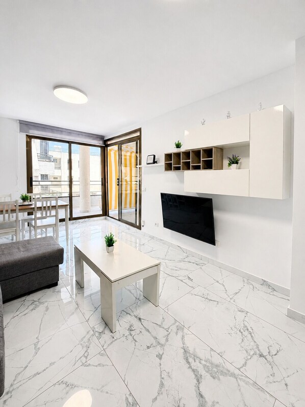 A modern living room with a flat-screen TV, a sofa, a coffee table, and a dining area with chairs.