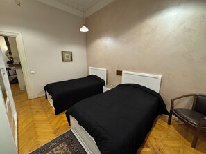 A bedroom with two single beds, a wooden floor, a chair, a bedside table, and a hanging light fixture.