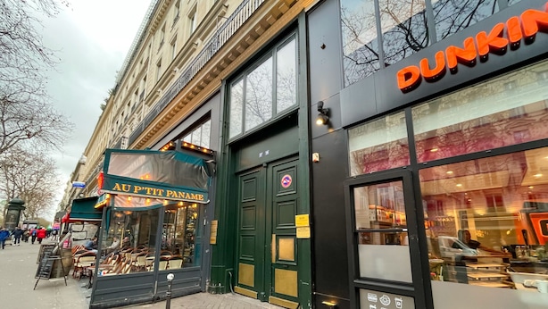 Ein Dunkin' Donuts mit sichtbarer Schaufensterfront und einem Schild für 'AUP'TIT PANAME' gegenüber.