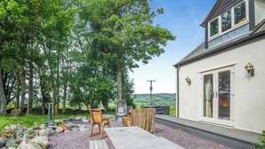 A patio with a table and chairs, surrounded by trees and a view of the countryside. - 4 bedroom accommodation in Betws-Y-Coed (Betws-Y-Coed)