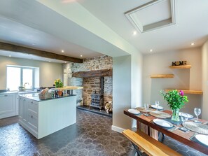 Una cocina con pared de piedra, vigas de madera, una isla central y comedor con mesa de madera para seis.