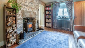 A cozy living room with a stone fireplace, a bookshelf, a blue rug, and a leather sofa. - 4 bedroom accommodation in Betws-Y-Coed (Betws-Y-Coed)