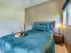 Un dormitorio con una cama grande, una mesita de noche, una lámpara y una ventana con cortinas.