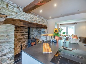 Una cocina con pared de piedra, estufa de leña, encimera de madera y un jarrón con flores.