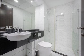Um banheiro moderno com pia branca, bancada preta e box de vidro.