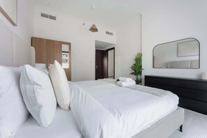 Quarto de hotel moderno com uma cama grande, um guarda-roupa de madeira escura, uma cômoda preta e um espelho grande na parede.