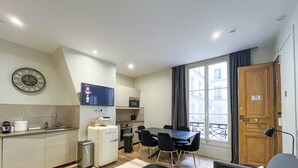 Una cucina moderna con microonde, forno e lavello. C'è una zona pranzo con tavolo e sedie. Un televisore è montato a parete sopra la cucina.