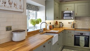 A modern kitchen with light green cabinets, a wooden countertop, a built-in oven, and a window with a view of greenery.