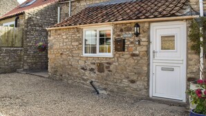 A stone building with a tiled roof, a white door, and a window with a white frame.