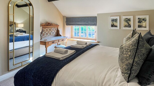 A bedroom with a large bed, a dresser, a mirror, and a window with a view of trees.