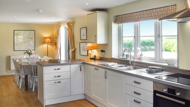 A modern kitchen with white cabinetry, a dining area with a table set for four, and a window with a view of greenery.