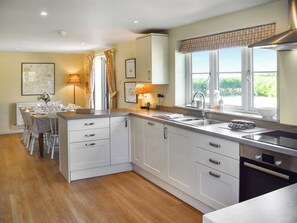 A modern kitchen with white cabinetry, a dining area with a table set for four, and a window with a view of greenery.