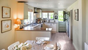 A modern kitchen with a central island, white cabinetry, and a dining area set for six with white chairs and a table set for a meal.
