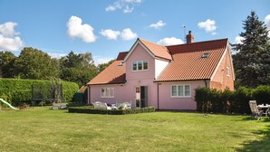 A pink house with a red-tiled roof, a grassy yard, and a play area with a slide.
