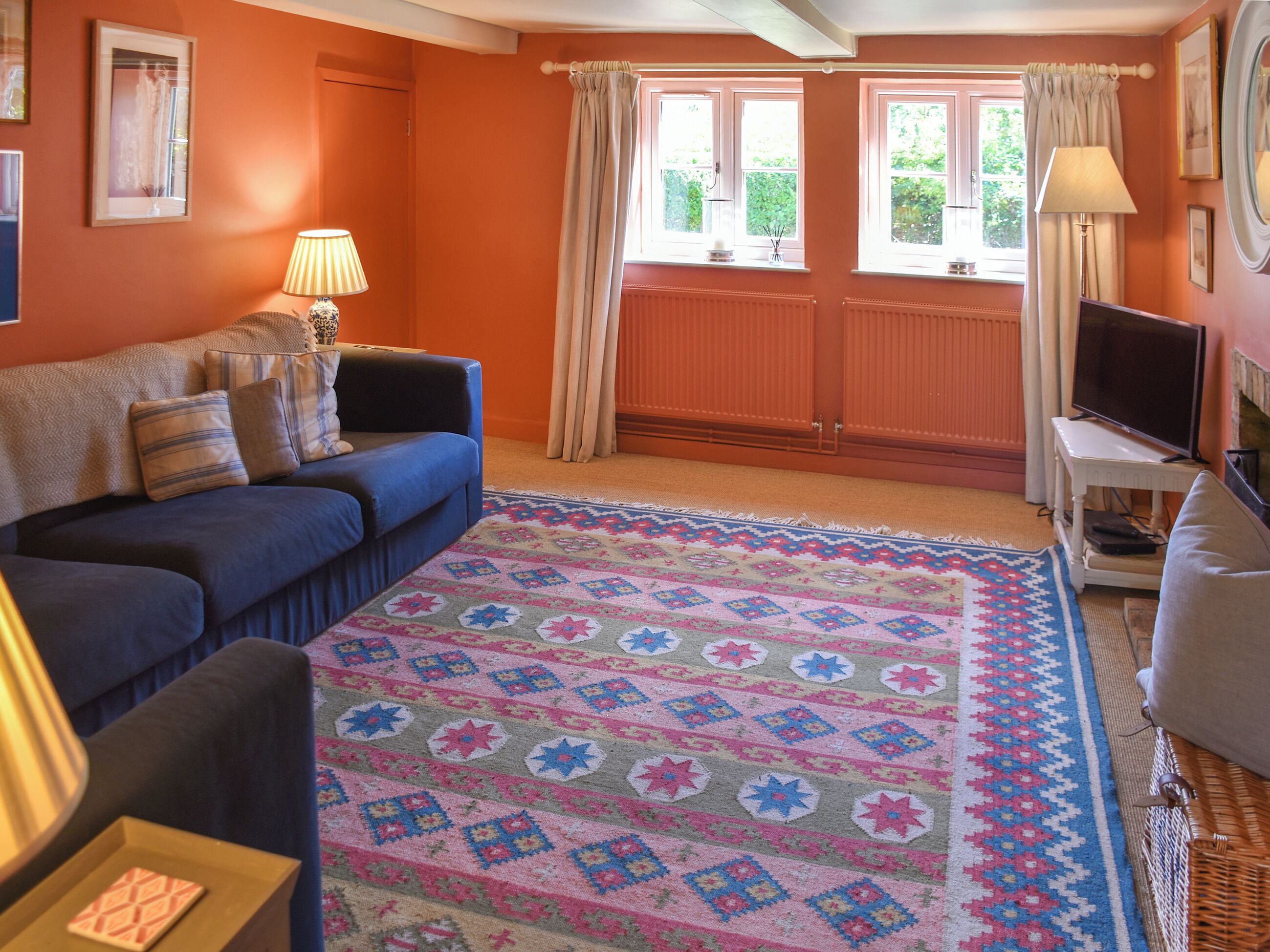 A cozy living room with a blue sofa, a patterned rug, and a television on a stand.