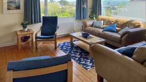 A living room with a sofa, armchair, and a small table with a bowl. - 4 bedroom accommodation in St Mawes (St Mawes)
