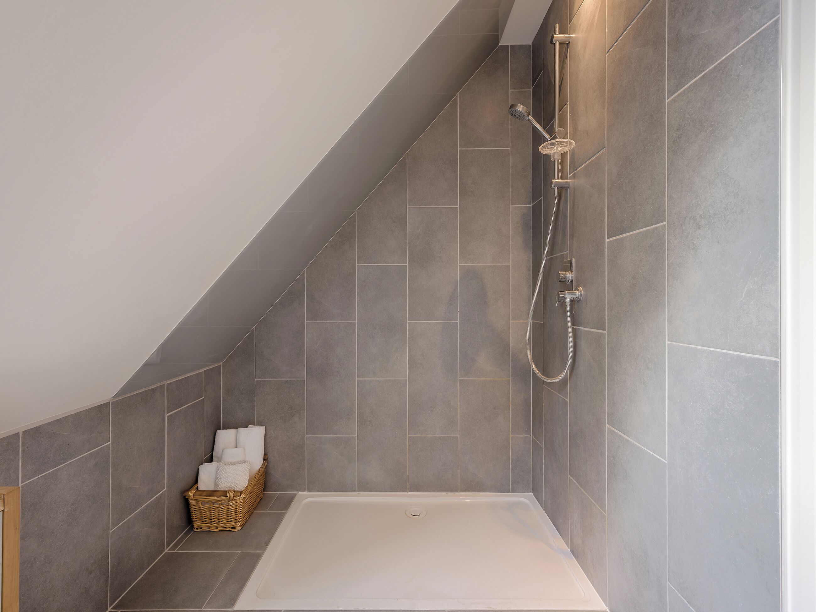 Une salle de bain moderne avec un plafond en pente, une douche équipée d’un pommeau de douche à main et une baignoire.