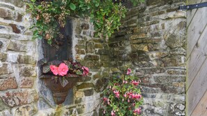 A stone wall with two hanging flower pots, one with pink flowers and the other with pink and white flowers. - 1 bedroom accommodation in Camelford (Camelford)