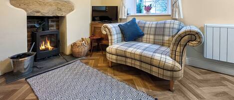 A cozy living room with a fireplace, a plaid sofa, a patterned rug, and a window with curtains.