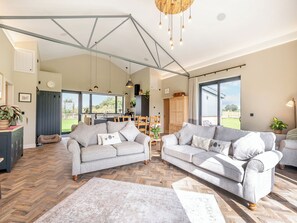 A spacious living area with a herringbone floor, two grey sofas, a dining table, and a kitchen in the background.