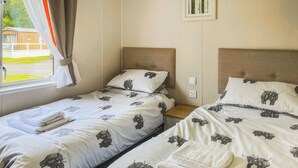 Et hotelværelse med to senge, hver med en sengegavl, et vindue med gardiner og en stikkontakt på væggen.