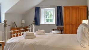 A bedroom with a bed, a window with curtains, a wooden wardrobe, and a desk with a lamp. - 4 bedroom accommodation in St Blazey (Par)