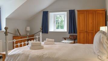 A bedroom with a bed, a window with curtains, a wooden wardrobe, and a desk with a lamp.