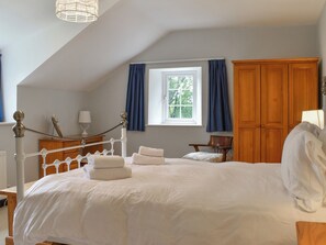 A bedroom with a bed, a window with curtains, a wooden wardrobe, and a desk with a lamp.