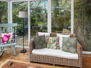 Un sofá de mimbre con cojines, una lámpara de pie y un sillón con un cojín floral.