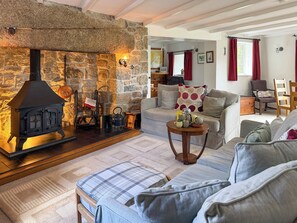A cozy living room with a stone fireplace, a sofa, a coffee table, and a chair. - 4 bedroom accommodation in St Blazey (Par)