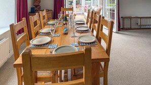 A dining table set for six with wooden chairs, a chandelier, and a view through a glass door. - 4 bedroom accommodation in St Blazey (Par)