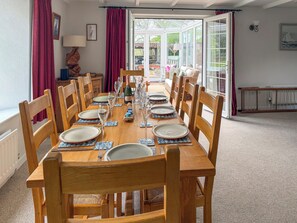 A dining table set for six with wooden chairs, a chandelier, and a view through a glass door.