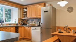 A kitchen with wooden cabinets, a stainless steel refrigerator, a dishwasher, a window, and a wooden bench. - 4 bedroom accommodation in St Blazey (Par)