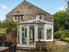 A stone house with a conservatory, a garden with potted plants, and a wooden deck.