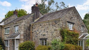 A stone house with a sloped roof, a chimney, and a gravel driveway. - 4 bedroom accommodation in St Blazey (Par)