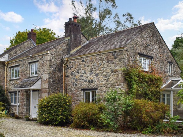 A stone house with a sloped roof, a chimney, and a gravel driveway.