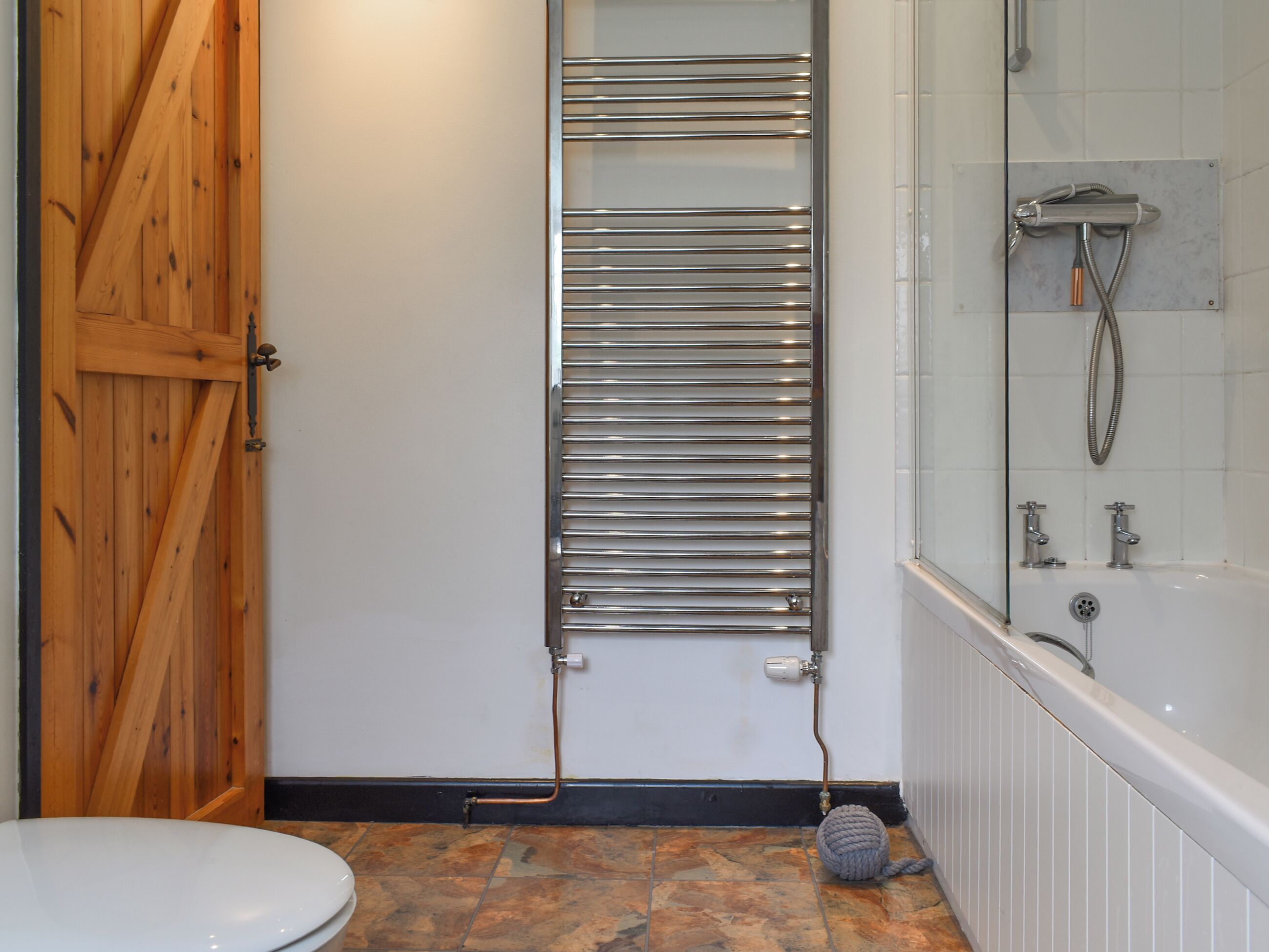 A bathroom with a wooden door, a towel rack, a shower, and a toilet.