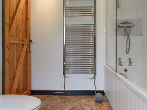 A bathroom with a wooden door, a towel rack, a shower, and a toilet.