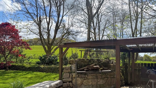 A stone patio with a pergola, a barbecue grill, and a view of a green field and trees. - 4 bedroom accommodation in St Blazey (Par)