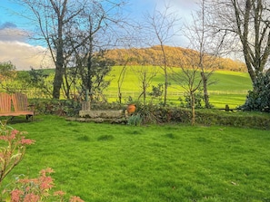 Un campo cubierto de hierba con un banco, árboles y una colina distante.