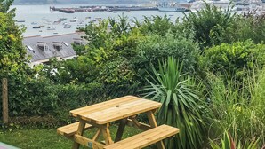 A wooden picnic table with benches in a grassy area with a view of a harbor.