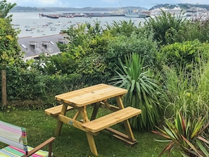 Une table de pique-nique en bois, avec des bancs, installée dans un espace verdoyant offrant une vue sur un port.