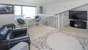 A modern living room with a sofa, chairs, a TV, and a staircase.