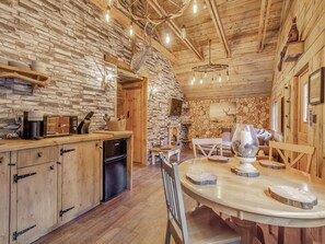 Ein rustikales Blockhaus-Interieur mit Steinwand, Holzbalken, einem Esstisch und einer Kaffeemaschine.