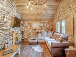 Un interior de cabaña acogedor con pared de piedra, pared de madera, techo de madera, un sofá y una chimenea.