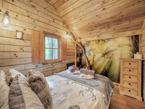 Dormitorio de cabaña de madera con cama, cómoda, ventana y un mural de bosque en la pared.