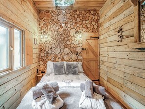Een houten kamer met een bed, handdoeken, een raam en een wand van boomstammen.